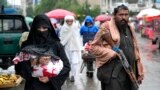 Kabul - o femeie afgană merge la piață în ținuta obligatorie - i se văd doar ochii și mâinile, în timp ce un luptător taliban stă de pază în Kabul (arhivă). 