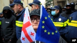 Жінка з прапорами ЄС та Грузії стоїть перед поліцейськими, які перегородили вулицю під час акції з вимогою провести нові вибори. Тбілісі, 25 листопада 2024 року